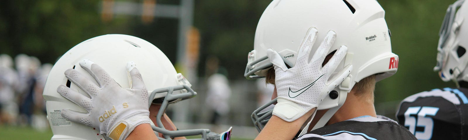 Color photo of two pre-teen boys in football pads and helmets, looking into each other’s eyes and encouraging each other.