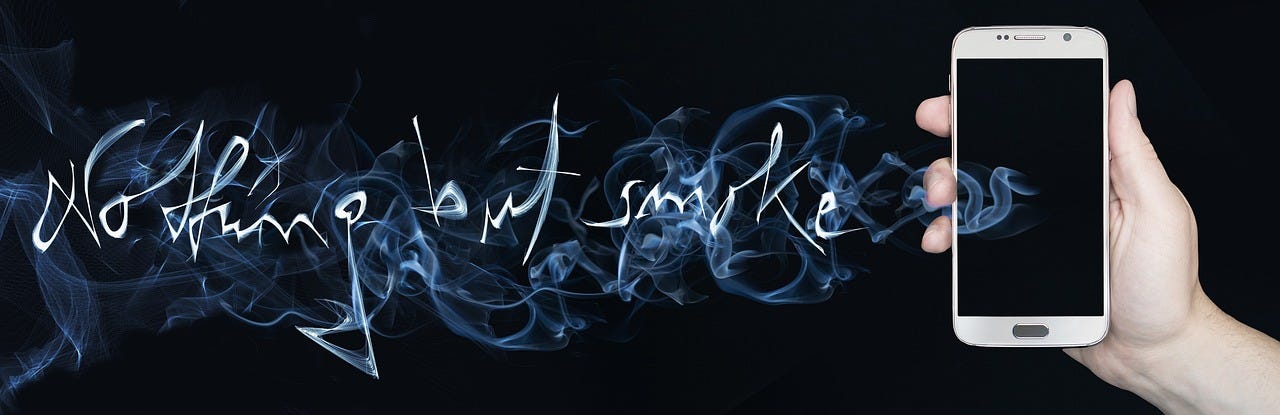 A hand holding a mobile phone and proceeding this hand is the words ‘Nothing But Smoke’ written in smoke tendrils.