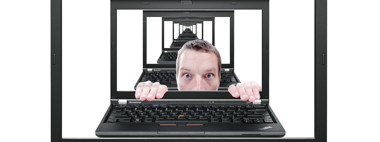 A frightened man looks out from behind a laptop