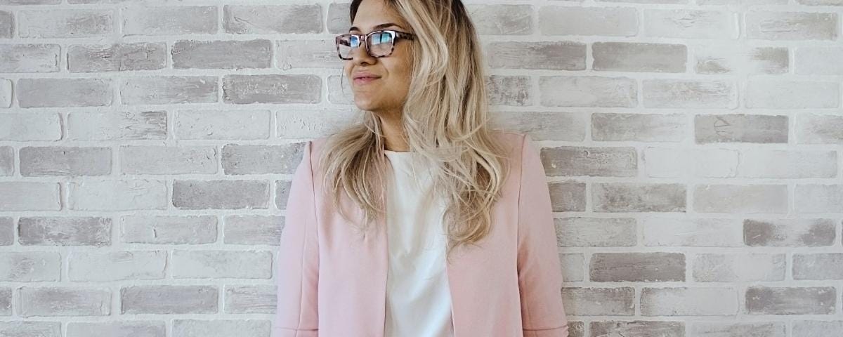 Woman standing in front of a brick wall wearing a pink cardigan