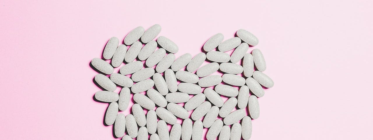 White heart made of pills on a pink background