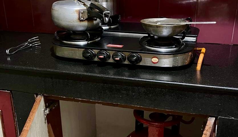 A red gas cylinder underneath a gas stove which is on a kitchen counter.