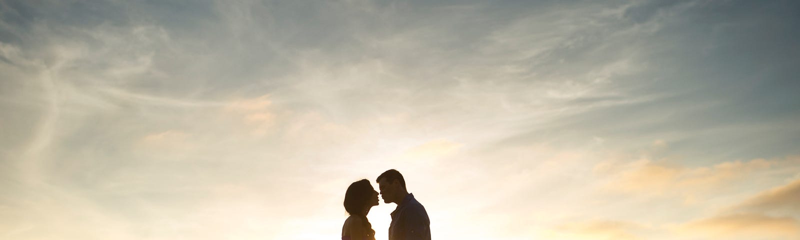 A couple overlooking the ocean at sunset, about to kiss.