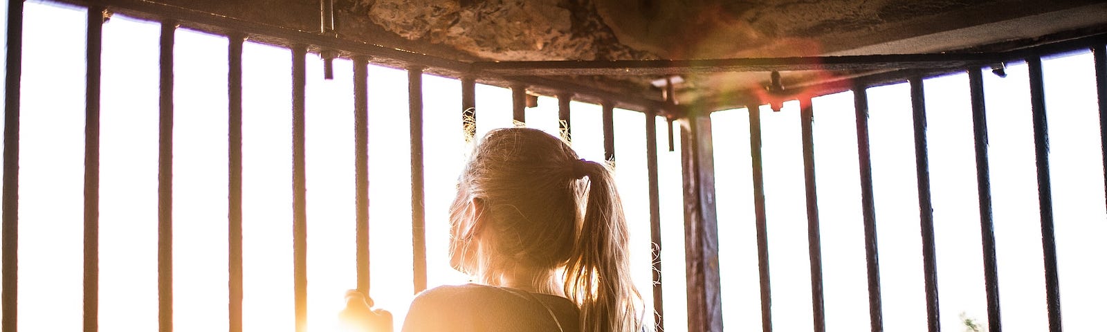 A woman looking at the sun from inside a cage.