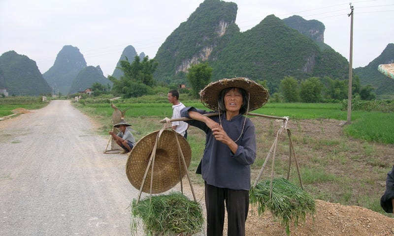 Three farmers on the road in Southern China’s Guangxi province. One is balancing two baskets filled with vegetables on pole. Fang-shaped karst-limestone hills in the background are found primarily in Southern China and Northern Vietnam.