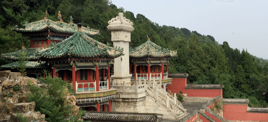 Traditional Chinese building with tiled roof in front of forested mountain