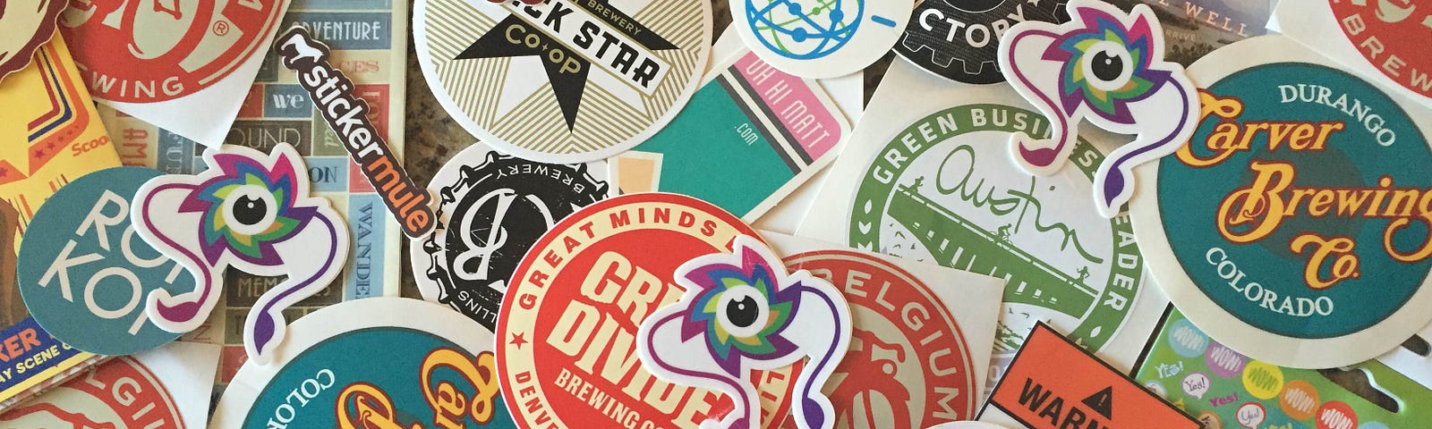 The photo shows a pile of colorful stickers from dozens of small and large companies including SeaLab Digital Design Agency.