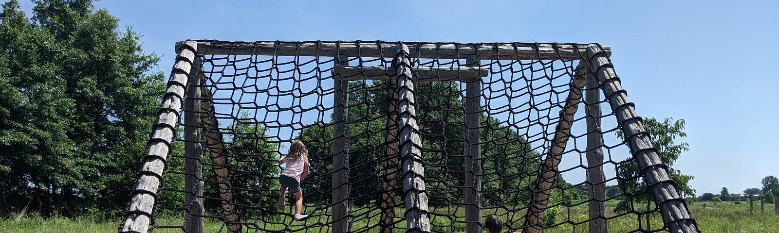 Boy and girl climbing up a rope wall at a challenge course outdoors.