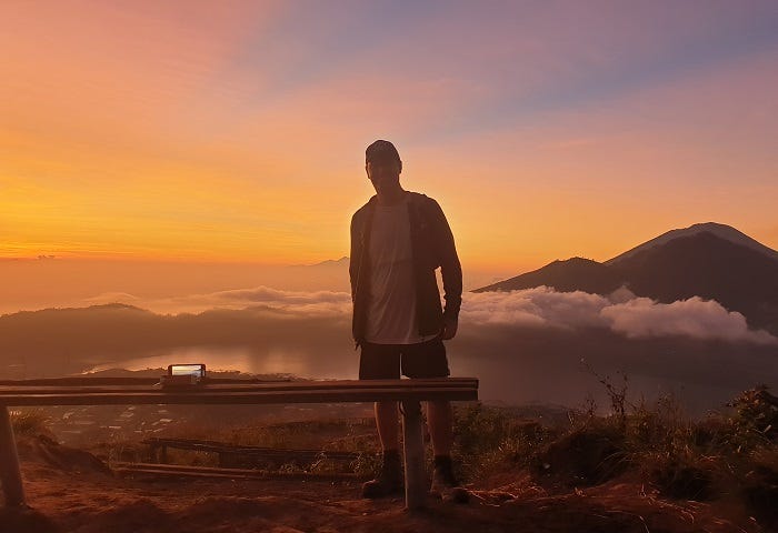 man standing with sunrise and mountains in background