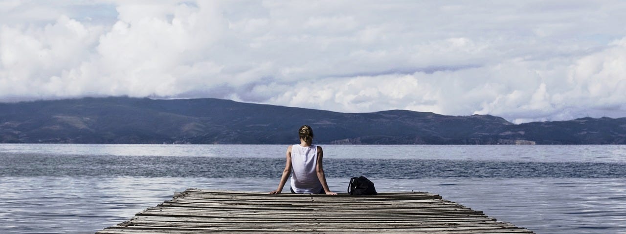 Woman sitting alone at the end of a pier by the water