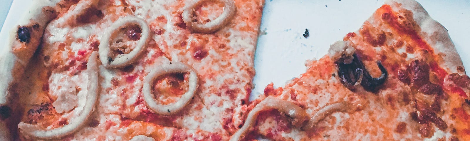 A pizza missing a slice in a box. The pizza is topped with seafood including calamari rings and tiny octopus.