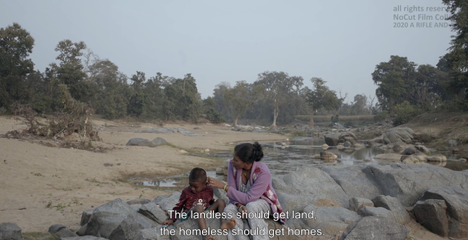 Film still from A RIFLE AND A BAG of Somi talking to her son, saying “The landless should get land and the homeless should get homes.”