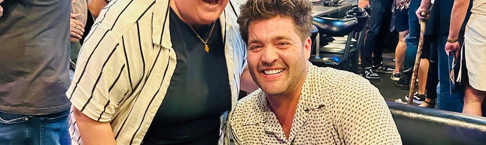 Wren Shealy (left) and CT Tamburello (right) share a fun moment at The Challenge Mania Live show in Zanies Rosemont. Wren is beaming while CT sits beside a signed Challenge poster, both caught mid-laugh during their unforgettable conversation about soup.