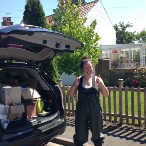 Dr Laura Carter smiling at camera with her thumbs up standing next to an open car boot packed full of boxes of equipment.