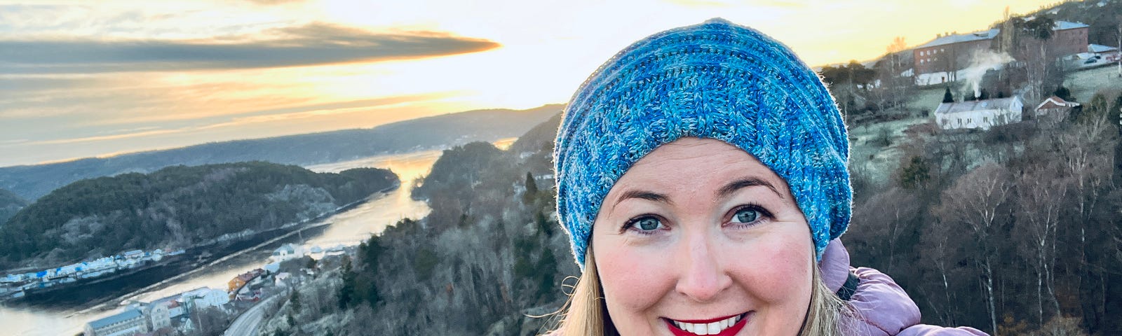 selfie of author in Halden, Norway with a scenic sunset background on a mountain with water below