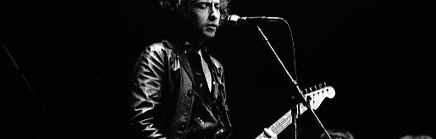 Image of Bob Dylan on stage singing and playing a Fender Stratocaster