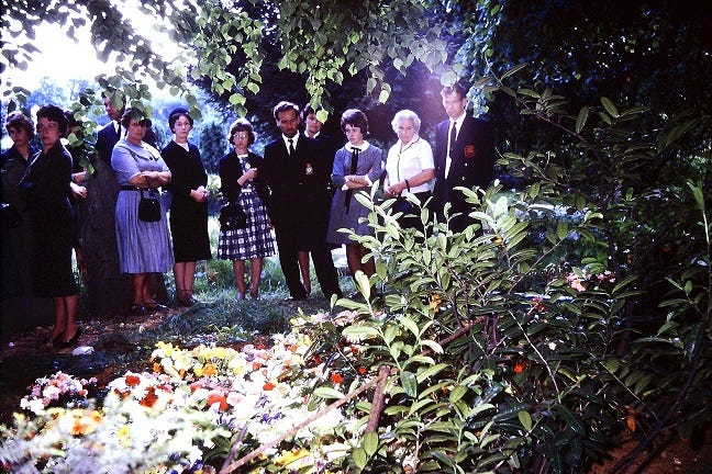 A line of people at a funeral standing behind a show of flowers