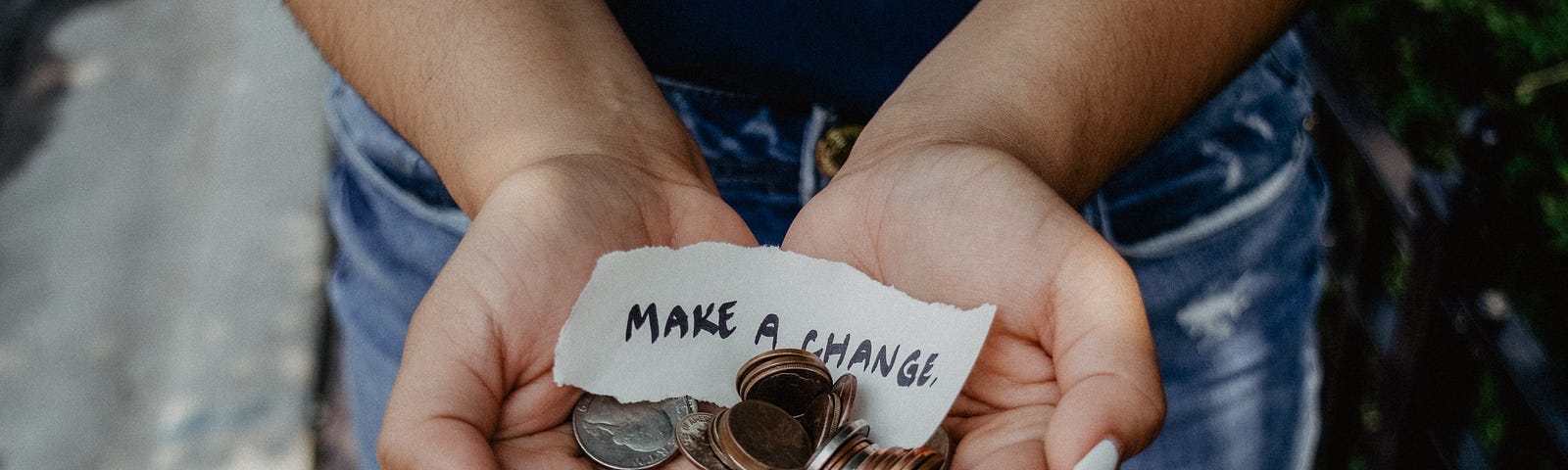 A woman standing on the sidewalk, holding change in the form of pennies and nickels, with a small note that says make a change