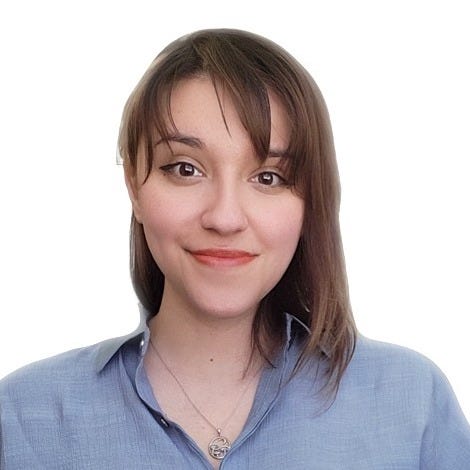 Photo of Alma, a Hispanic woman, from the shoulders up. She is facing directly into the camera with a closed-lip smile and curtain bangs framing her brown eyes. Her brown hair is straight and shoulder-length. She is wearing a collared, light blue button down shirt. She has winged eyeliner, peach lipstick, and a silver mushroom necklace.