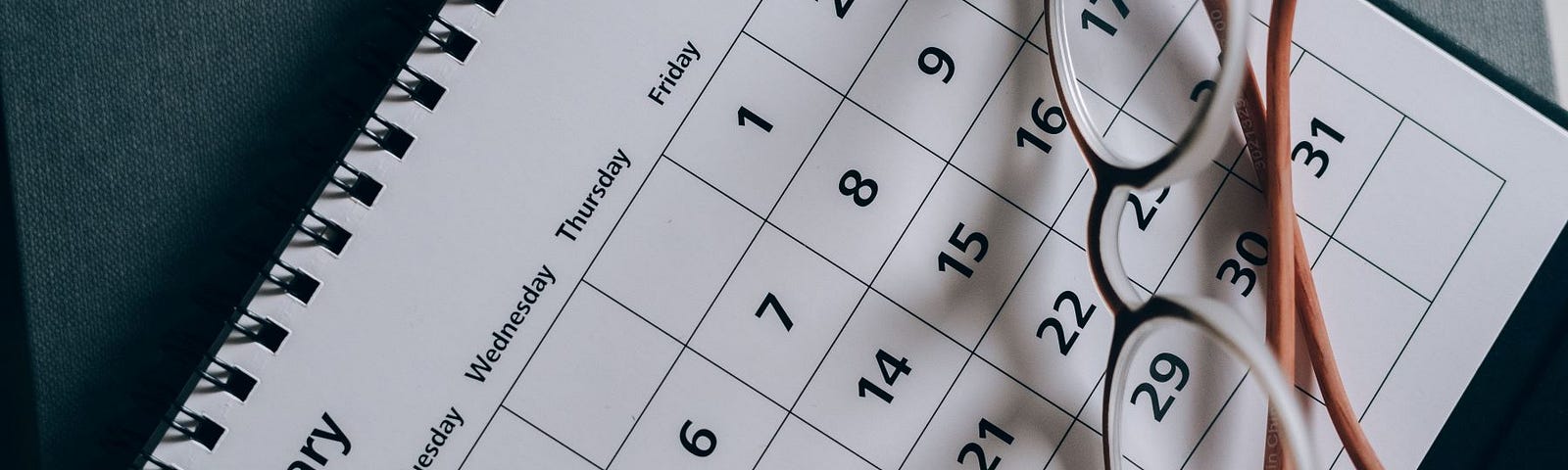 A calendar open to the month of January, with folded glasses sitting on it.