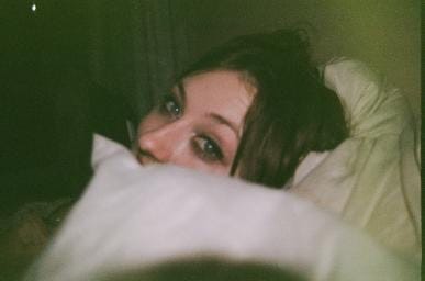 A film photograph of a woman’s eyes over a pile of pillows.