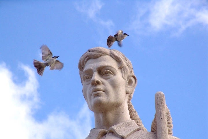 Granite sculpture closeup of a man’s head with two birds circuling it.