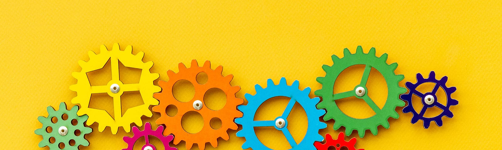 A number of different-sized and coloured cogs sit interconnected on a background of yellow