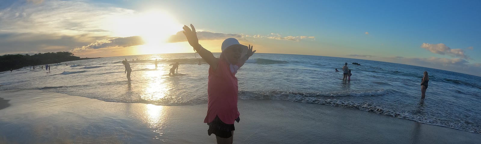 Author’s Mom waving her arms at sunset on a beach.