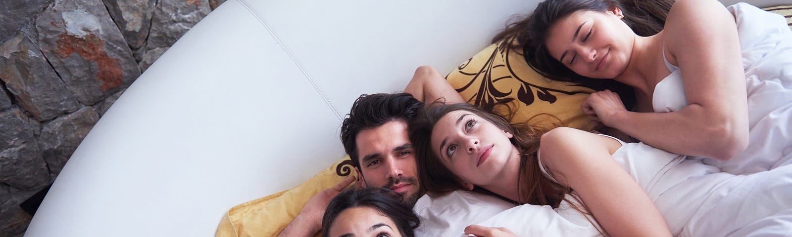 Three women and a man enjoying time in bed together.