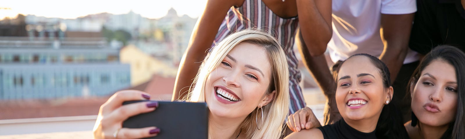 young blonde woman taking a selfie on a rooftop with her group of friends.