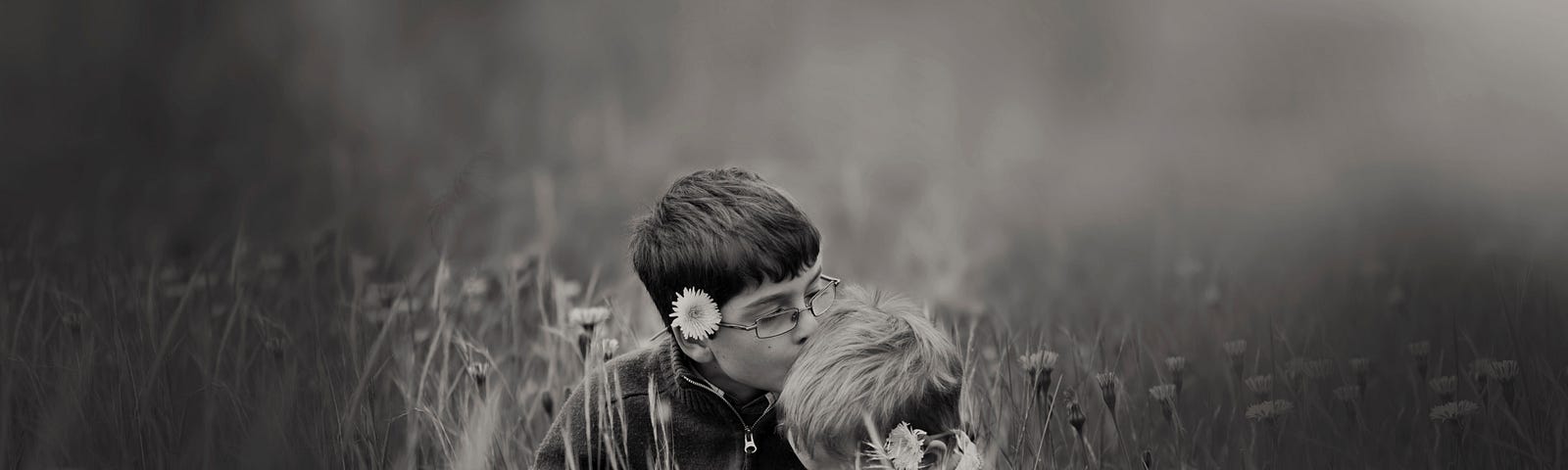 Boy kissing a younger boy’s head in a field surrounded by flowers