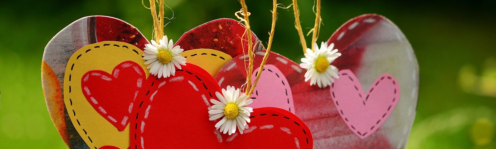 A bunch of colorful hearts, decorated by daisies, hanging together from a string.