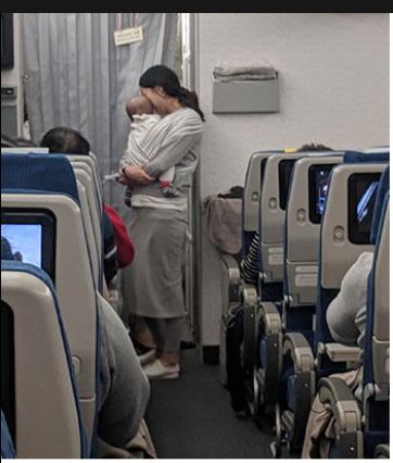 The Korean mile with a baby cradled standing on the aisle talking to a fellow passenger