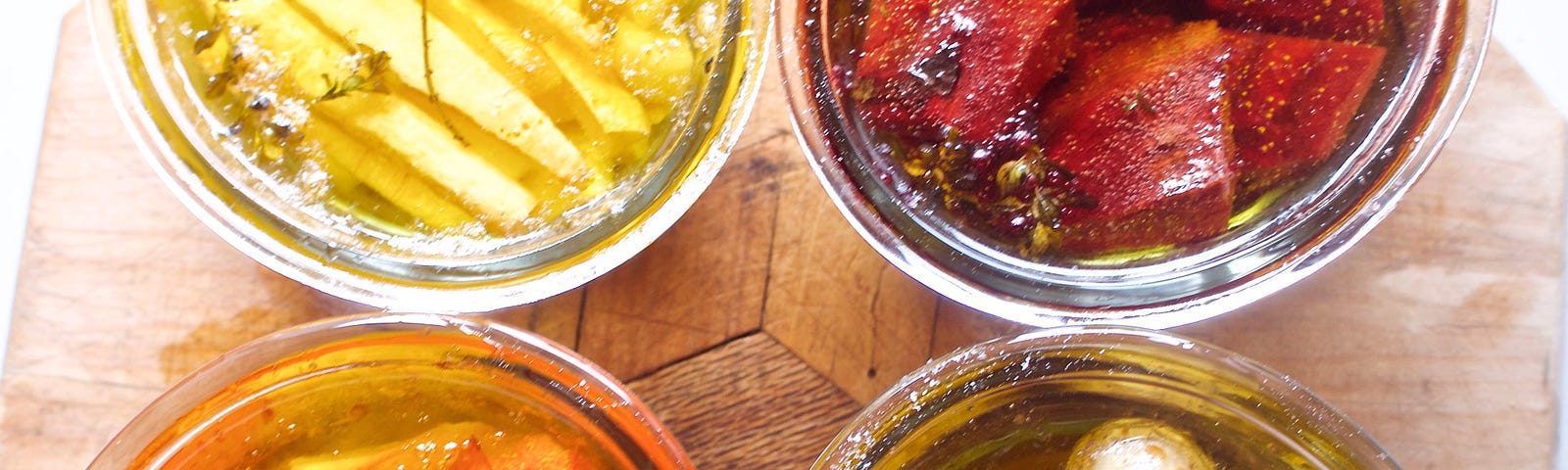 four jars of oil and confit’d veg — parsnip, beet, tomato, and potatoes — in rich color