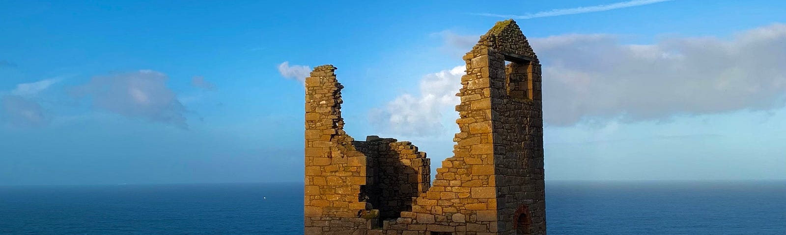 The top half of a ruin beside the sea catches the morning sun.