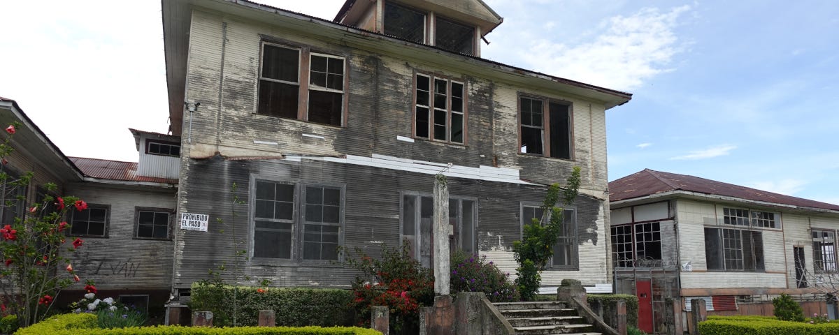 An abandoned sanatorium ward with broken windows, peeling gray walls, and no trespassing signs.