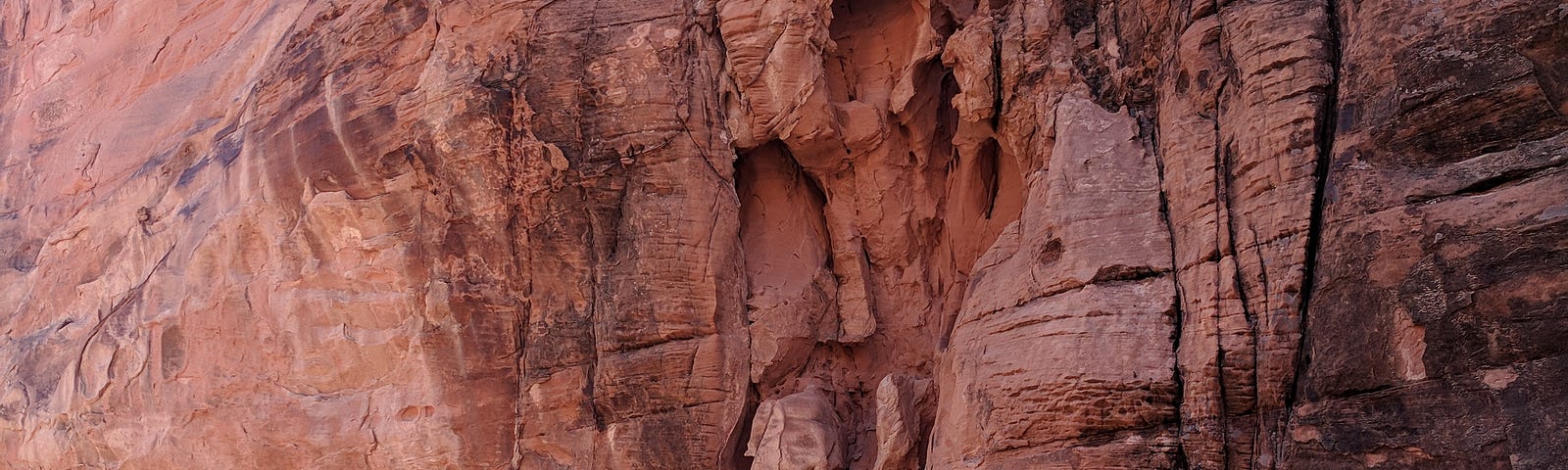 A woman reaches up to a red rock that looks likean animal’s head looking down with a smile.