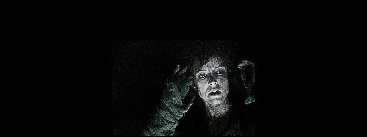 The face of a women appear shocked. Darkness surrounds her.