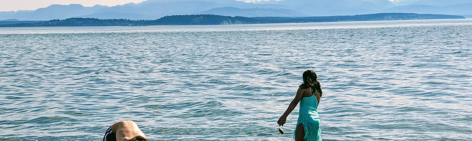 Two children playing in rocks and sand at the water’s edge.