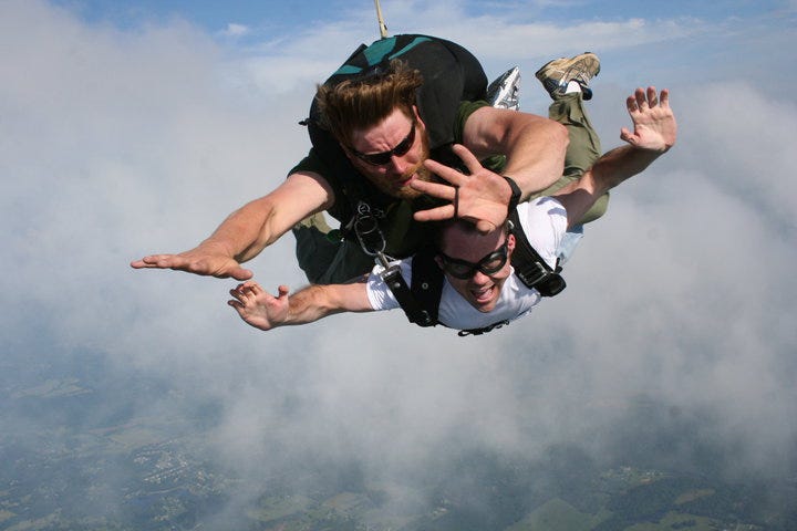 Two people tandem skydiving with Earth visible below clouds