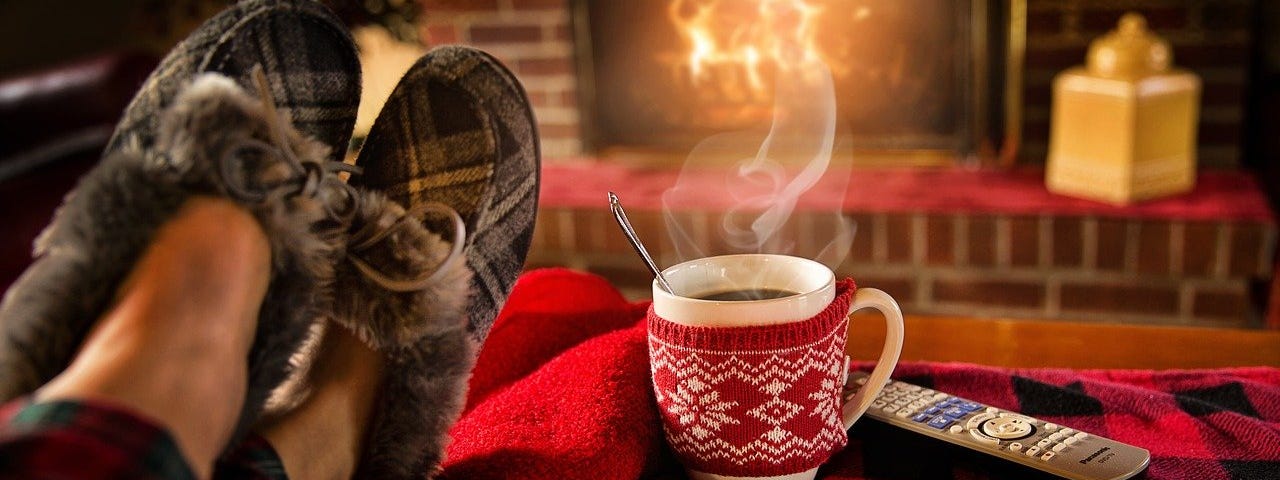 Recharge your mind and body/by Laura Knapke/Medium.com Picture of someone wearing slippers relaxing in from of a fire with a cup of coffee.