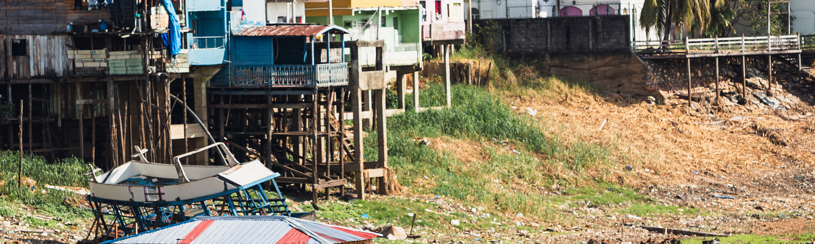 The image shows a riverside community in the Amazon Basin experiencing the effects of severe drought. The riverbed is mostly dry, exposing boats that are stranded on the ground. The houses, some of which are built on stilts, indicate that the area usually experiences high water levels. The dry conditions illustrate the drastic impact of droughts on these communities, affecting their transportation, access to goods, and overall way of life. This visual evidence underscores the findings of the rec