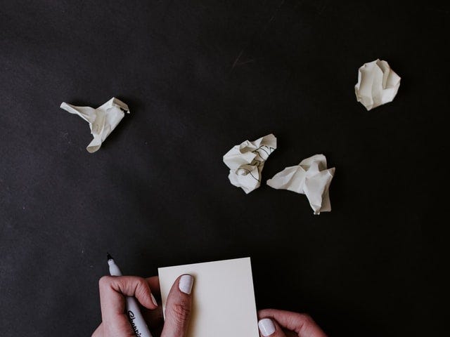 hands holding a permanent marker and sticky note pad with crumpled sticky notes above