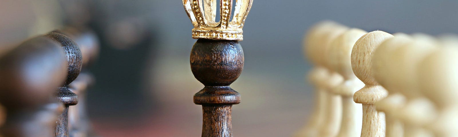wooden chess pieces in background, queen piece with golden crown in focus