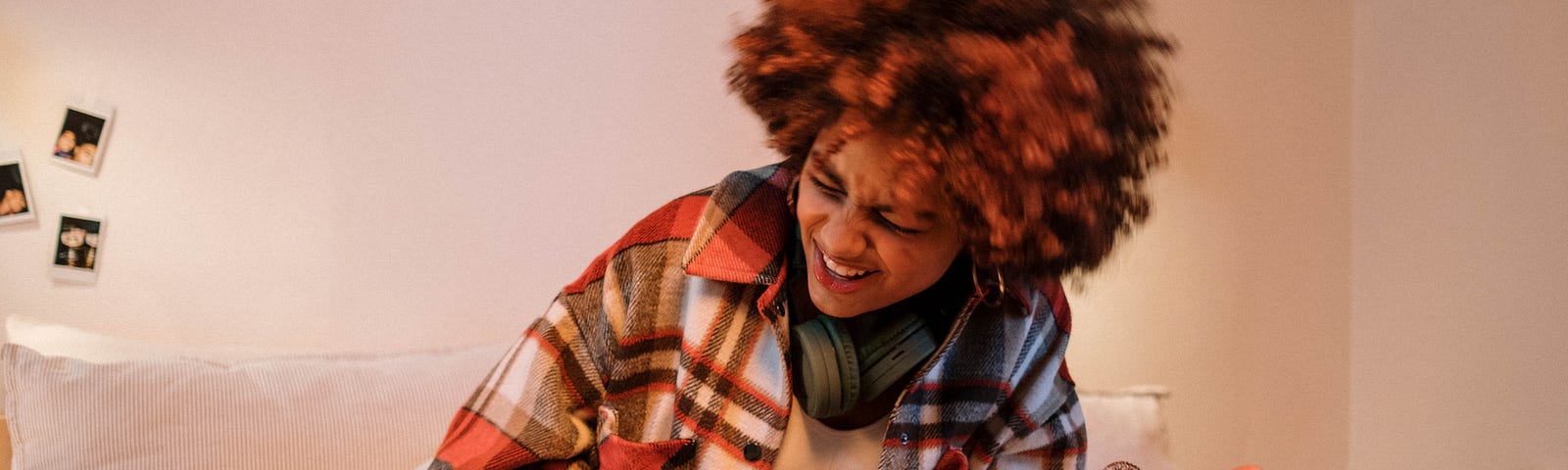 A woman with a multi-colored afro rocking out while sitting on her bed.