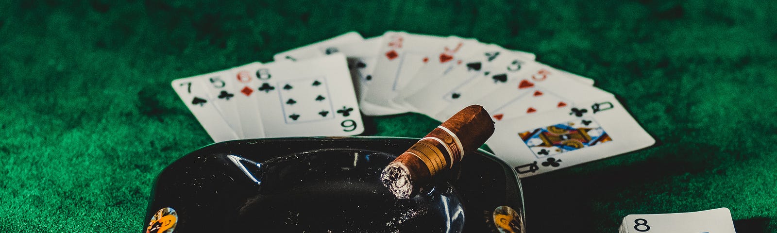 Cigar resting on an ash tray on a cards table, with cards spread out on the table.