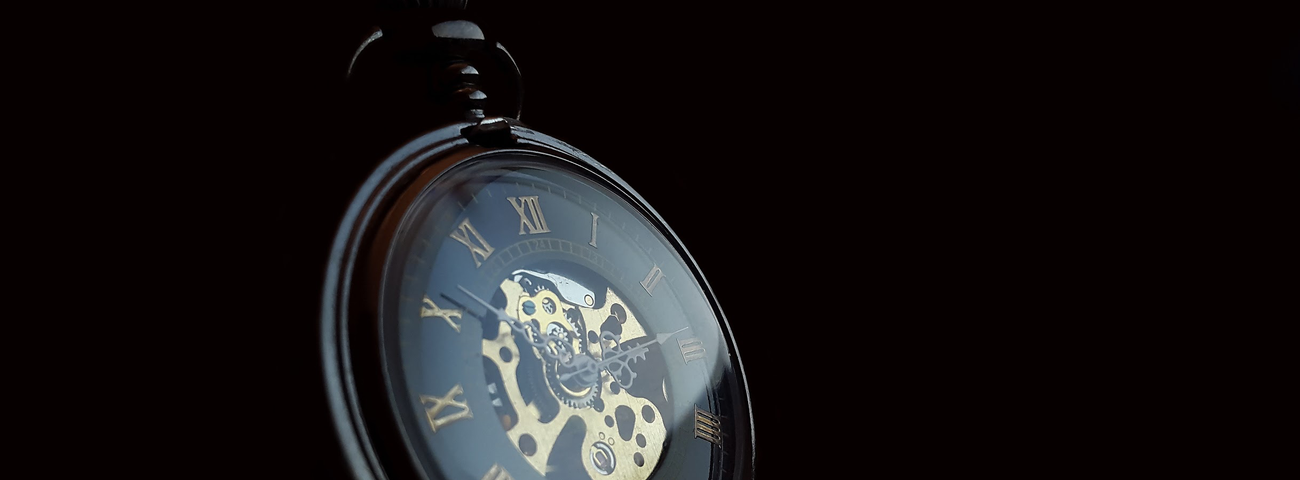 Image: A  black and gold pocket watch against a  plain black background.