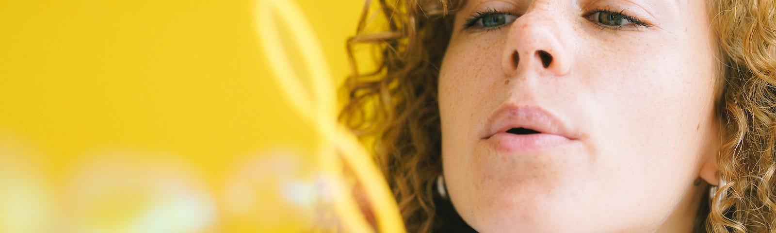 Adult woman blowing bubbles against yellow background.