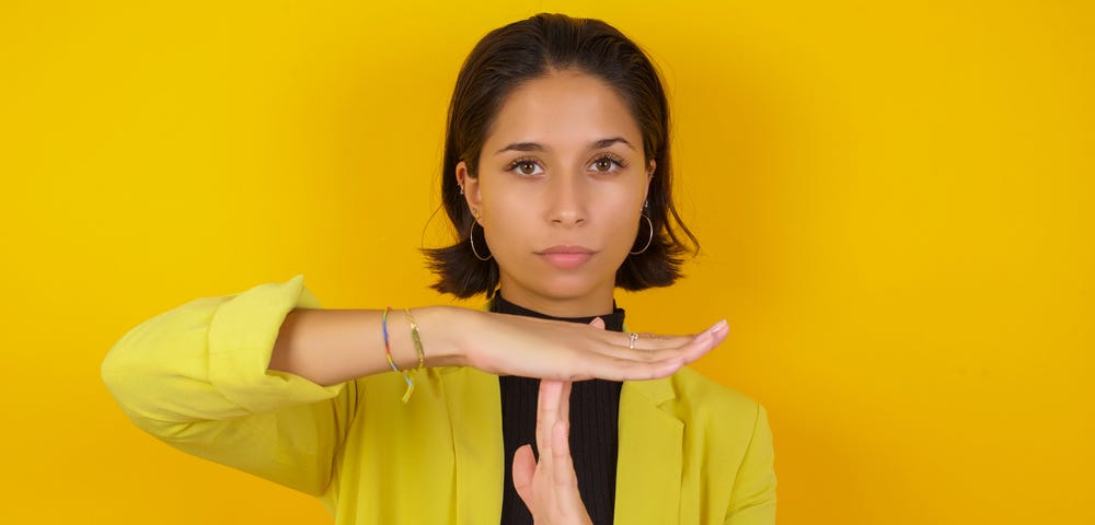 Woman dressed in business casual attire with hands in a “time out” sign