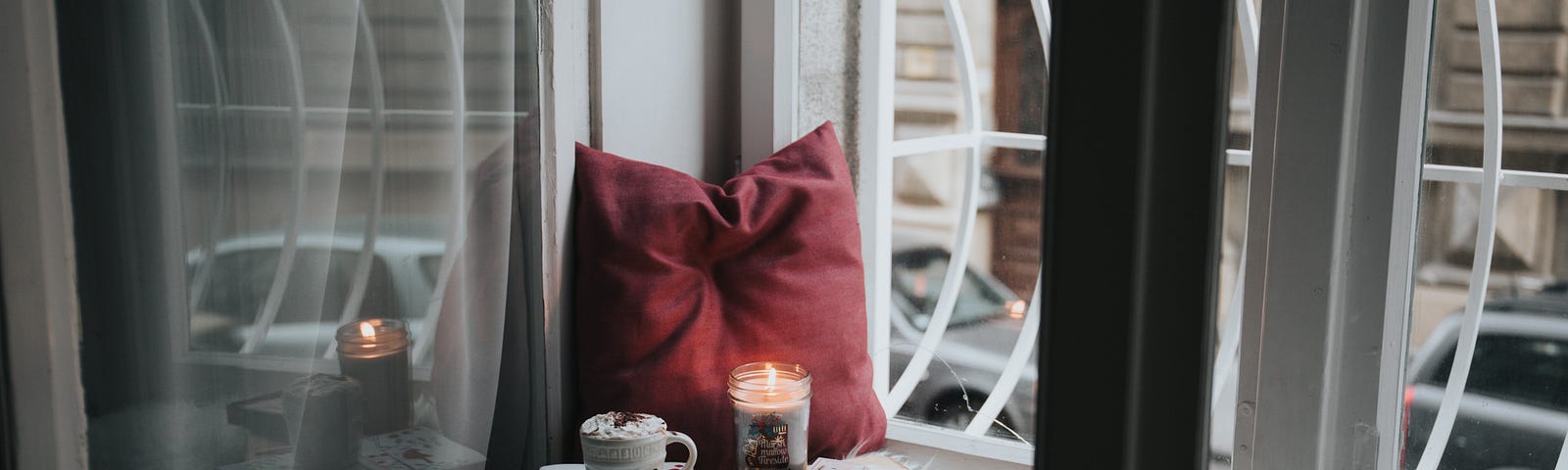 a pillow, candle, mug and books in a corner by a window